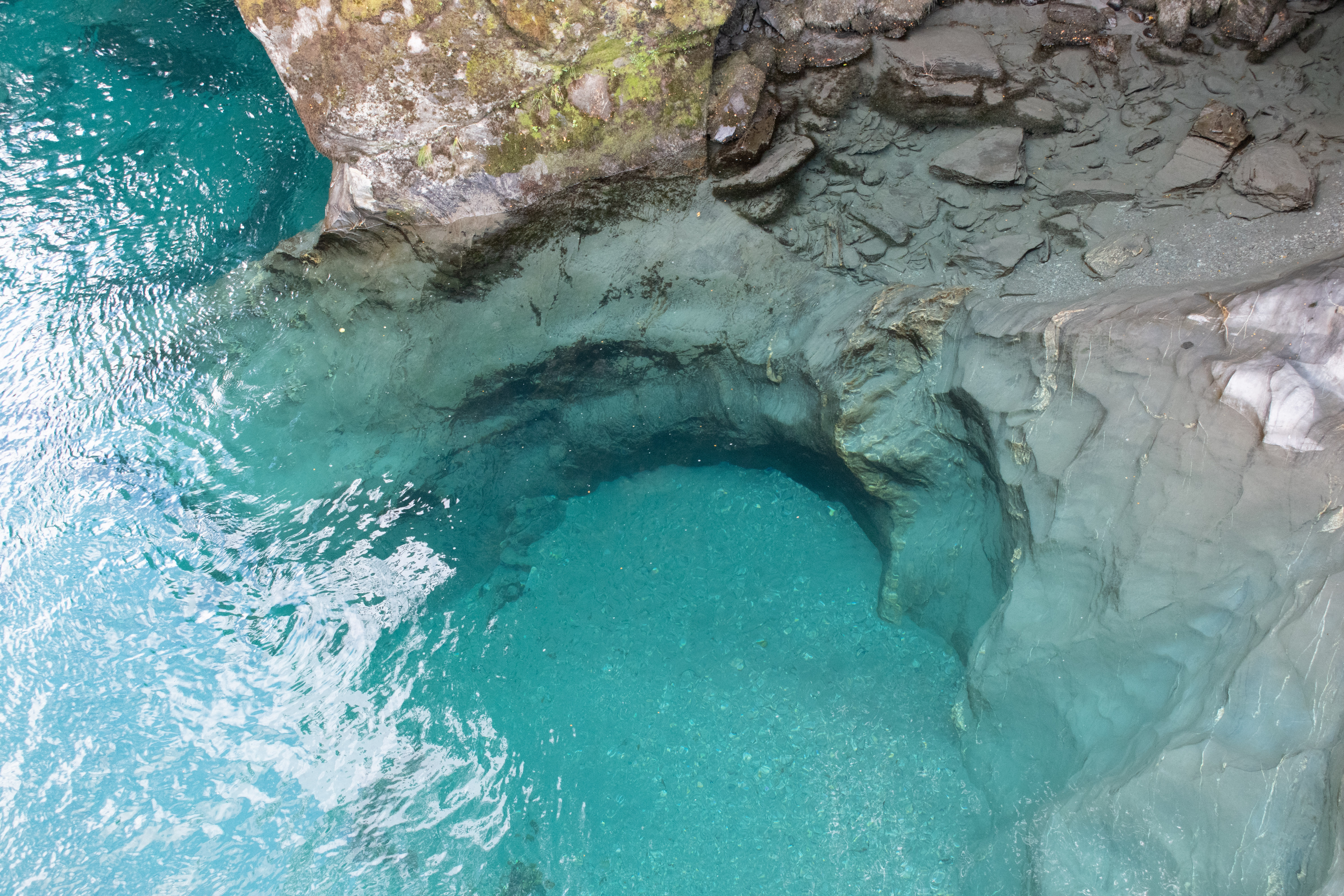 An aerial view of the dramatic blue pools. Round coves can be seen where the water has carved the cliffs on either side of the tributary, the water flowing down from the mountains into the broad river downstream.