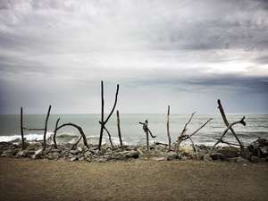 A stylized sign made of driftwood spells "Hokitika" on the West Coast shore of New Zealand, looking out to the Tasman Sea.