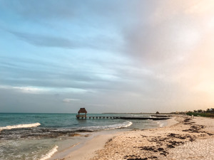 A small pier juts out into the Caribbean Sea between Mexico's Playa de Carmen and Cancún, at the Mayan Palace and Grand Mayan luxury resorts along the Riviera Maya. Clouds reflect the setting sun over the turquoise-blue water and white sand.